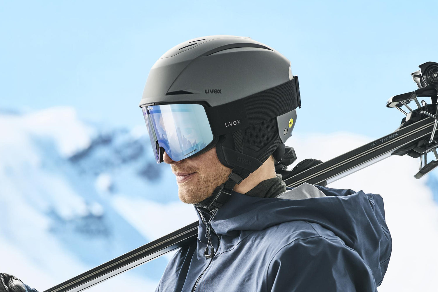 Person holding skis and ski poles with a snowy mountain background