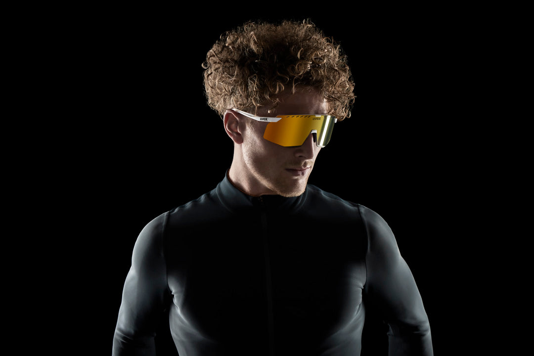 a man wearing uvex pace stage cv sunglasses and a black skin-tight shirt with a black background