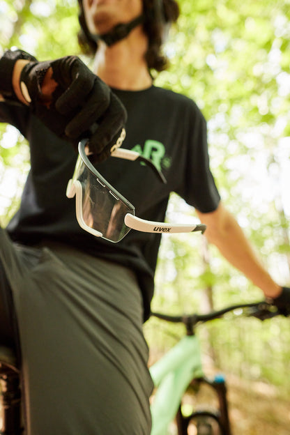 a gloved hand holding uvex sportstyle 236 s sunglasses with clear lenses